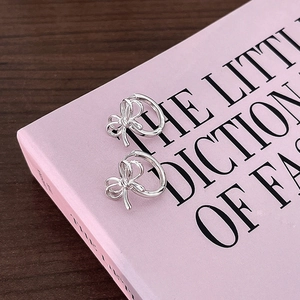Close-up of silver bow hoop earrings placed on a pink fashion book over a dark wooden table