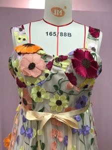 Détail de broderies florales 3D et nœud en satin sur robe de soirée beige en mesh
