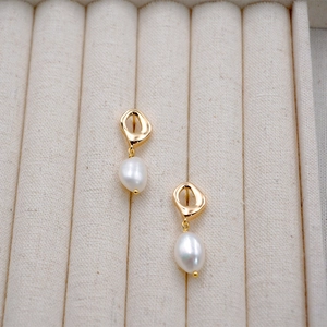 Baroque irregular pearl drop earrings with golden geometric hooks on cream fabric