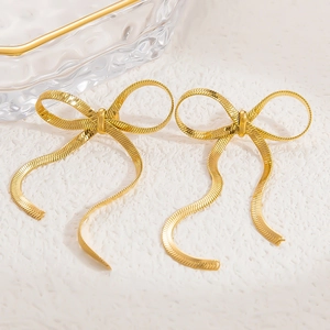 Macro detail of golden ribbon bow earrings featuring delicate metallic texture