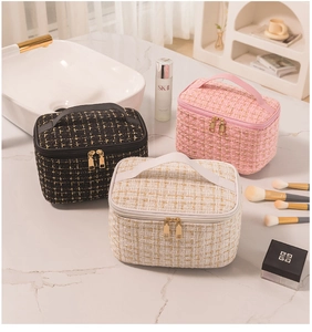 Three elegant tweed makeup bags in black, pink, and cream with gold zippers on marble