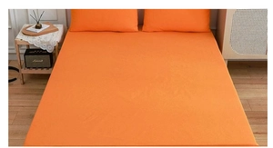 Detail of vibrant orange fabric fitted sheet and pillowcase set in a bedroom setting