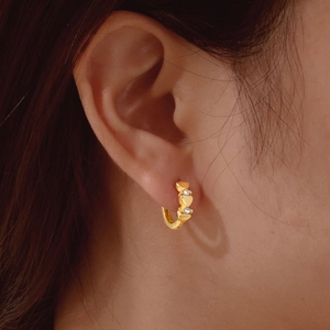 Close-up of golden huggie earrings with heart relief and tiny white zircons on a model