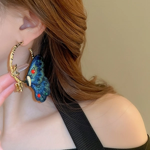 Detail of embroidered blue butterfly earrings with gold metallic frame worn by a model