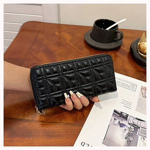 Close-up of quilted black leather wallet with gold zipper detail on a coffee table