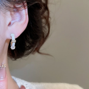Detailed close-up of a cream enamel C-shaped hoop earring with gold accents and diamonds