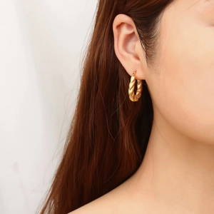 Close-up of a model wearing large golden twisted rope hoop earrings in stainless steel