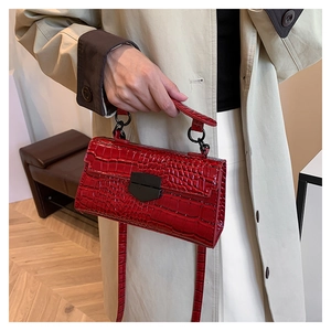 Detail view of red crocodile embossed handbag with black metal clasp held by hand