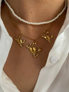Detail of gold crab pendant necklace layered with pearls on a white shirt