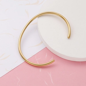 Detail view of gold open cuff bracelet on white stone and pink textured background
