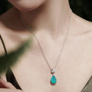 Close-up of a pear-cut blue gemstone necklace worn against a luxury silk garment