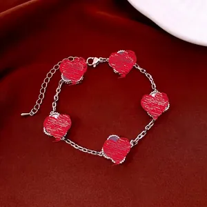 Détail du bracelet en argent avec cinq cœurs perlés sur un fond en satin rouge