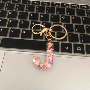 Detail of letter J keychain made of resin with colorful heart sequins and gold lobster clasp