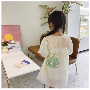 Detail of light green girls' crossbody bag with pearl handle and cartoon texture