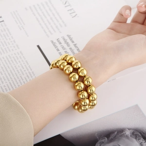 Detail of a minimalist gold beaded elastic bracelet set worn on a female wrist