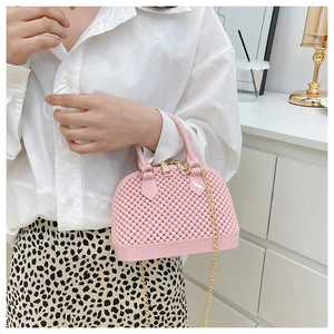 Close-up of pink jelly shell bag with woven texture and gold chain strap held by model