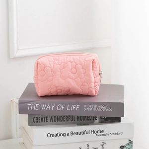 Close-up of pink quilted floral cosmetic bag with silver zipper on decorative books