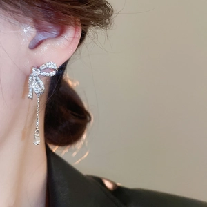 Macro shot of silver bow earrings with sparkling cubic zirconia tassels on a model
