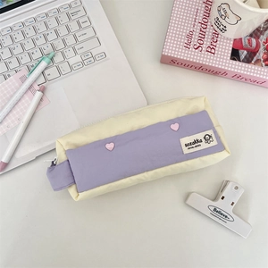 Detailed view of color-block pencil case with pink heart buttons on a desk setup