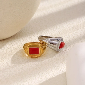 Close-up of gold and silver signet rings with rectangular red stone on textured surface