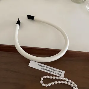 Minimalist white faux leather headband with black end tips on a vintage tray with pearls