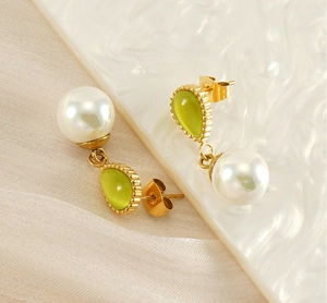 Détail de boucles d'oreilles dorées asymétriques avec perles et pierres œil de chat