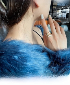 Detail of gold olive leaf ring with white enamel on a model hand with blue faux fur