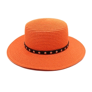 Détail d'un canotier en paille orange vif avec bande en cuir noir et rivets métalliques argent
