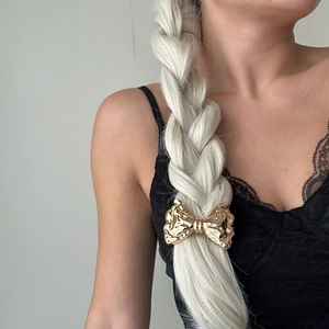 Detail of a golden metal bow hair clip with hammered texture on a braided ponytail