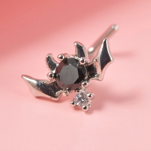 Macro shot of a silver bat-shaped nose stud featuring a black stone and clear gem