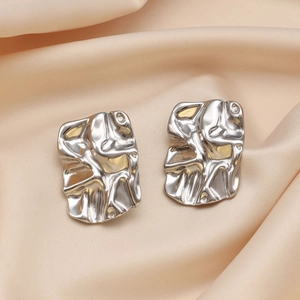 Macro detail of silver crumpled rectangle stud earrings on elegant beige silk fabric