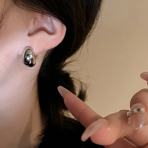 Macro view of polished silver water drop stud earring on a model ear with minimalist style