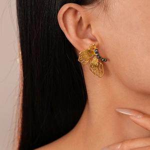 Close-up of golden butterfly earring with hollow wings and dark beads on model's ear