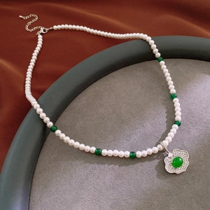 Macro detail of natural pearl and green bead necklace with ornate silver padlock pendant