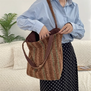 Detail of soft brown faux fur tote bag with green stripes worn by a model in a home setting