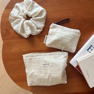 Three-piece beige textured fabric storage set with scrunchie and zipper pouches on wood