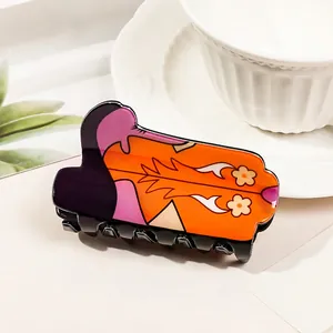 Detail of a bright orange acrylic cowboy boot hair claw with floral and flame motifs