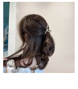 Golden twisted metal hair claw clip with rhinestones worn on a model's long wavy hair