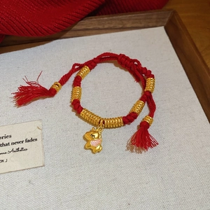 Dettaglio del bracciale a corda rossa intrecciata con perle dorate e ciondolo cavallo