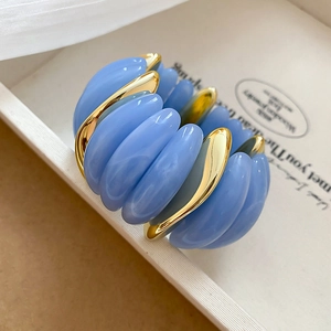 Macro detail of sky blue acrylic oval segments and gold wavy metal bracelet texture
