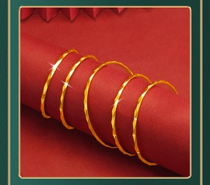 Detailed view of stackable gold geometric bangles on a red cylindrical display stand