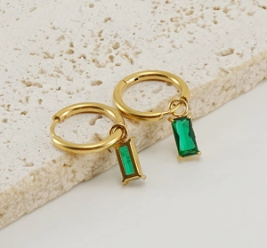 Détail de créoles en acier doré 18K avec pendentifs rectangulaires en zircone verte