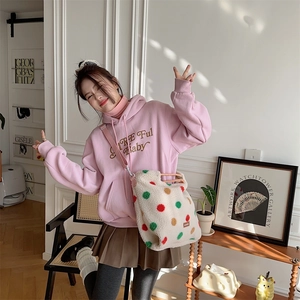 Detail of white plush striped crossbody bag paired with a pink embroidered hoodie