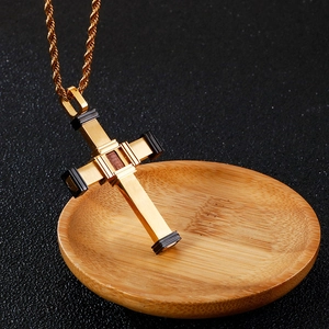 Macro shot of gold stainless steel cross pendant with dark wood inlay on a wooden tray