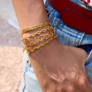 Close-up of four-piece gold bracelet set including snake and heart chains on wrist