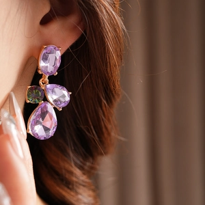 Close-up of vintage gold earrings with purple gemstones and crystals on model