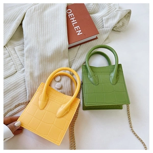 Close-up of yellow and green mini crocodile pattern handbags with metal chains