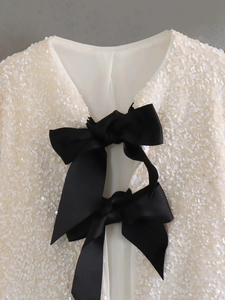 Detail of white sequin jacket featuring black satin bows and shimmering texture