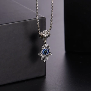 Macro shot of silver Hamsa hand necklace with blue evil eye pendant on black display