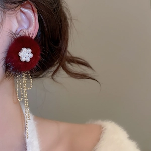 Close-up of elegant red fur ball earrings with pearl flowers and long gold tassel drops